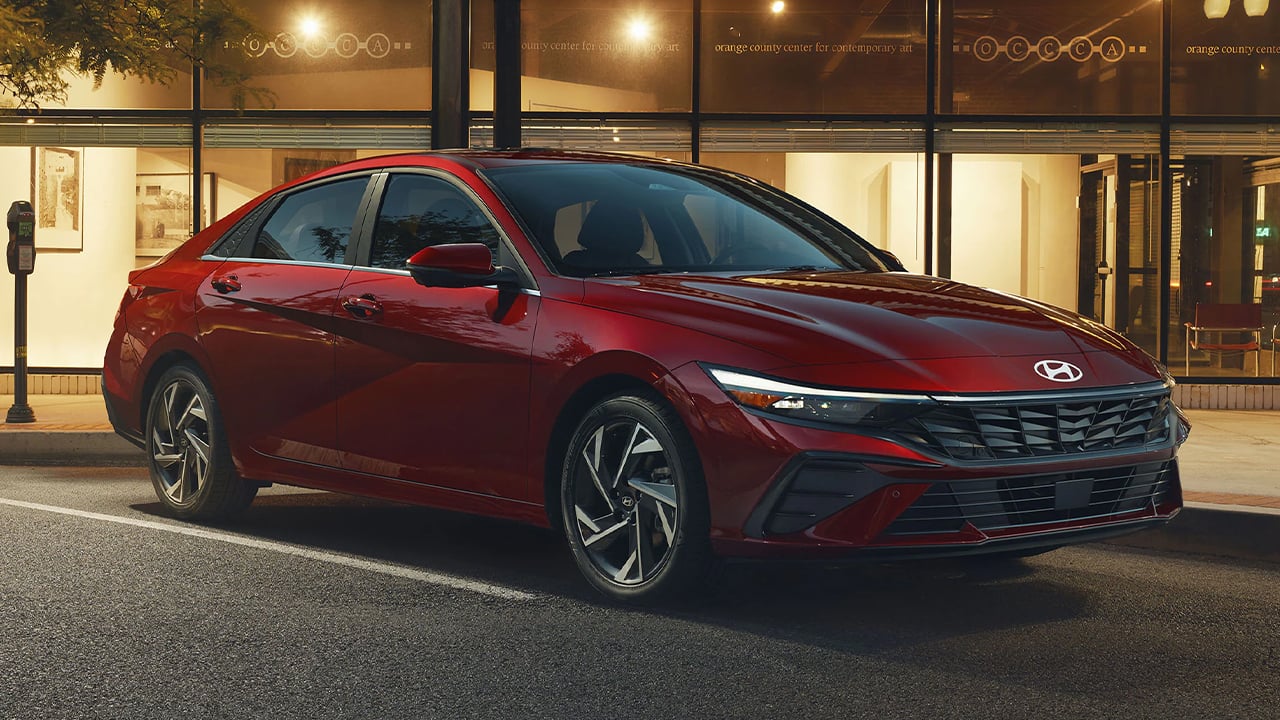 Vue 3/4 avant et latérale du Hyundai Elantra 2026 garé le soir dans un stationnement devant un batîment publique