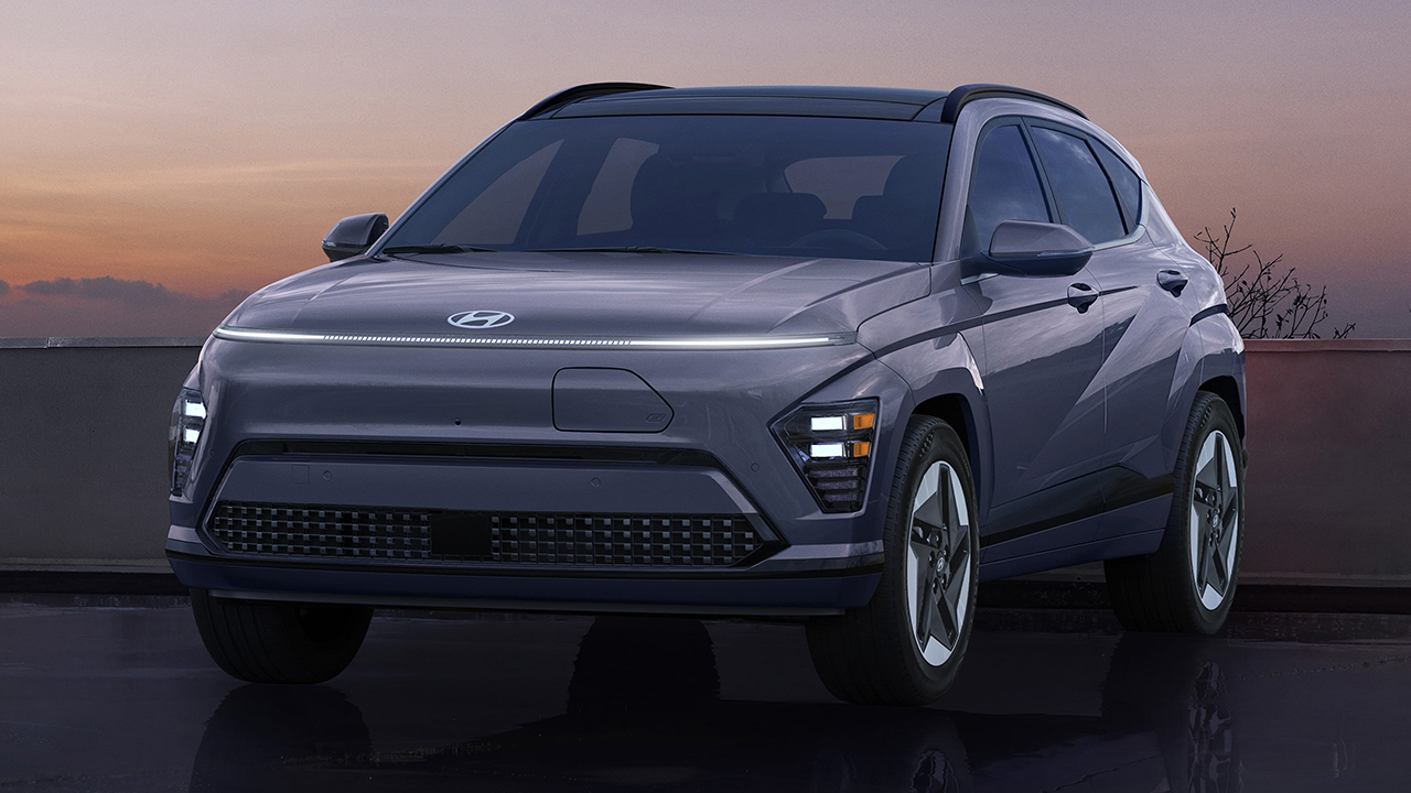 Vue 3/4 avant et latérale du Hyundai Kona électrique 2026 en arrêt dans un stationnement avec coucher de soleil et phares allumées