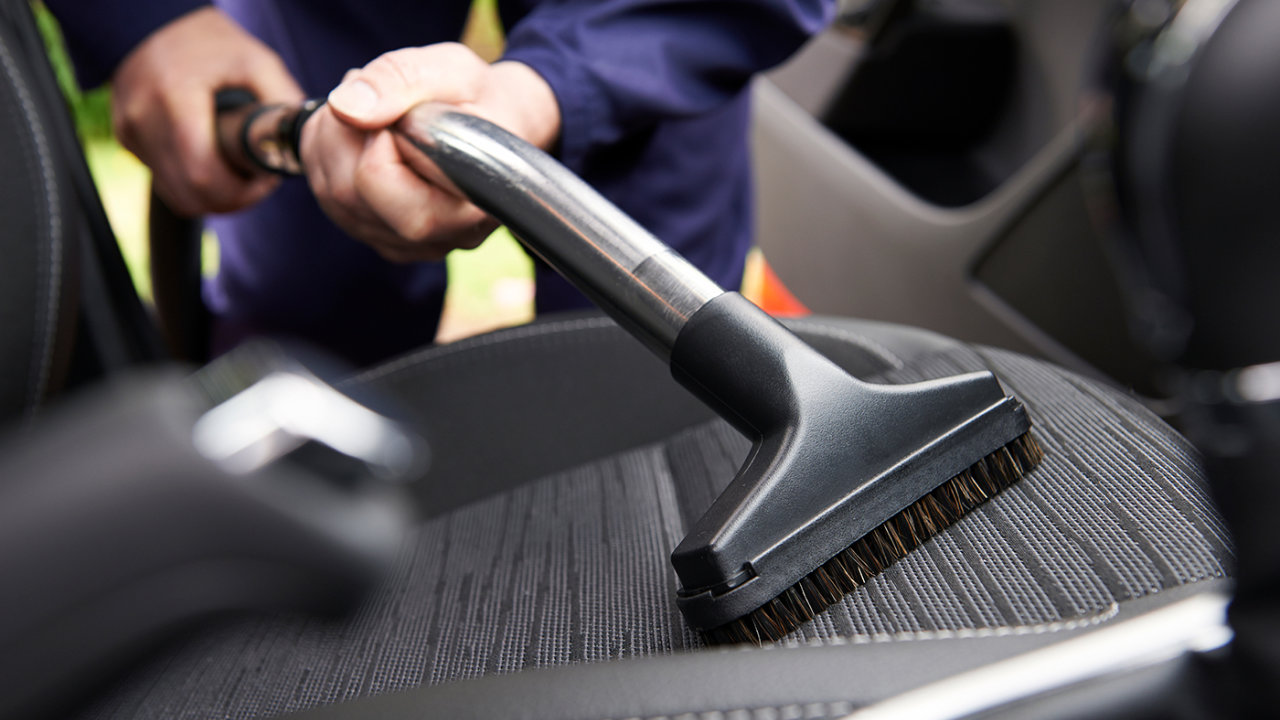 personne en train de passer l'aspirateur sur les sièges d'un véhicule