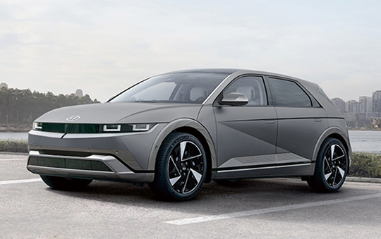 A gray Hyundai Ioniq 5 parked in a waterfront lot, shown from the front side with a city skyline in the background.